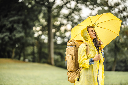 Female beautiful young tourist holding yellow umbrella, wearing yellow raincoat and enjoying in nature