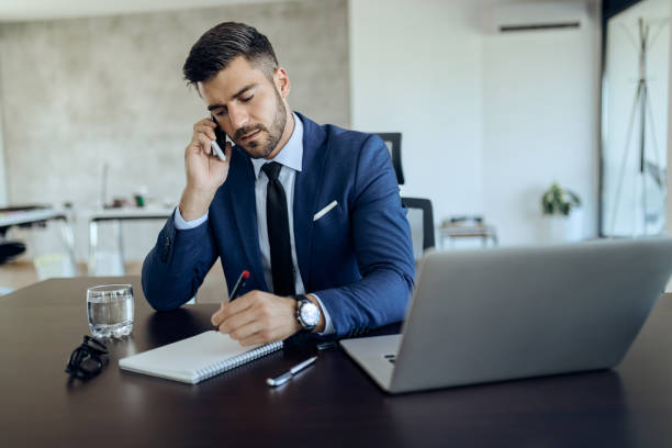 istock Young businessman writing notes while talking on the phone in the office. 1271163787