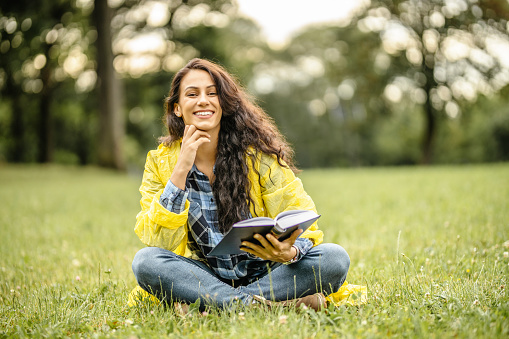 Happy woman in yellow raincoat reading a book in nature