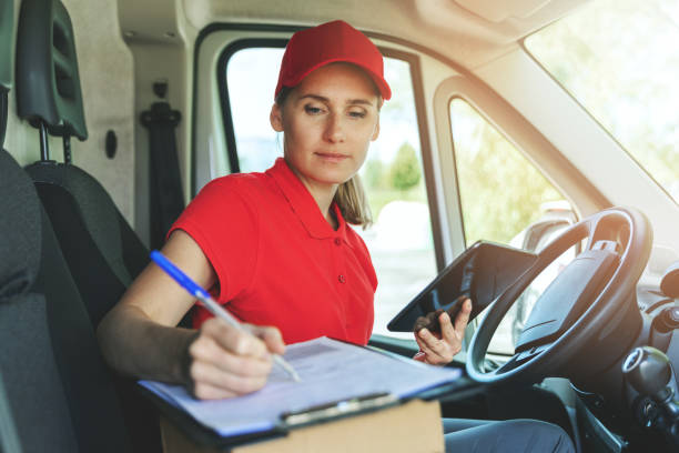 istock delivery person in red uniform sitting in van and writing documents on clipboard 1271168560