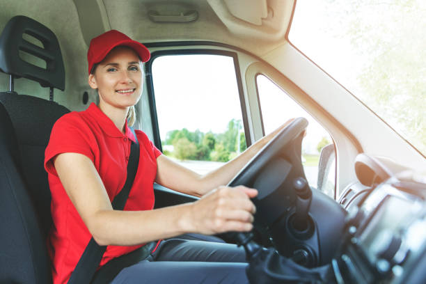 istock transportation services - young female driver in red uniform driving a van. smiling at camera 1271168586
