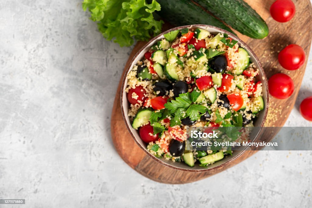 Salad with couscous and vegetables in a bowl on a gray concrete background Salad with couscous and vegetables in a bowl on a gray concrete background top view. Copy space. Tabbouleh of couscous, tomatoes, cucumbers, parsley and olives. Arabic or African cuisine. Couscous Stock Photo