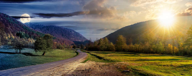 day and night time change concept above country road in valley. wonderful autumn landscape in mountains with sun and moon. forest on hills in colorful foliage. dramatic sky