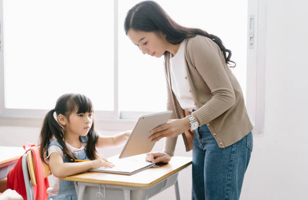 giovane insegnante asiatica che aiuta studentessa con tablet digitale in classe informatica. istruzione, scuola elementare, apprendimento e concetto di tecnologia. - korea child baby asian culture foto e immagini stock