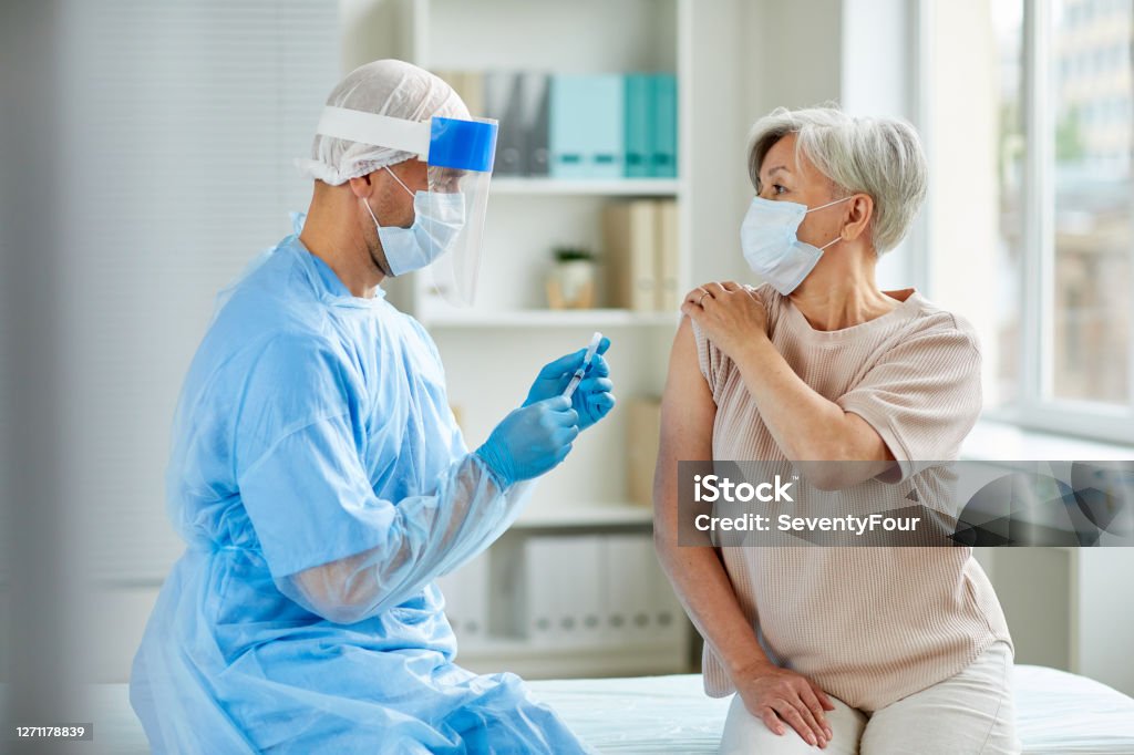 Male Nurse Preparing Injection Side view shot of male nurse wearing protective mask and gloves preparing medical syringe for giving injection to senior patient Vaccination Stock Photo