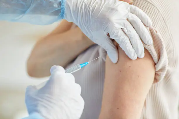 Close-up shot of unrecognizable doctor wearing latex gloves giving Covid-19 vaccine injection into womans shoulder