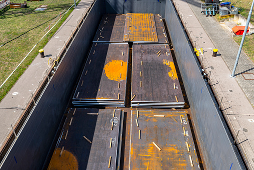 Barge filled with sheets of thick metal, flowing into the river lock, top view of the cargo holds of the ship.