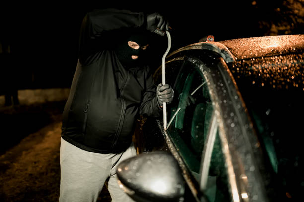 istock A robber dressed in black holding crowbar at a driver in a car. Car thief concept. 1271183254