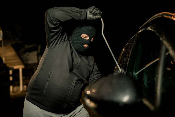 istock A robber dressed in black holding crowbar at a driver in a car. Car thief concept. 1271183323