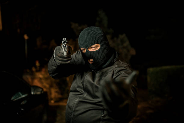 Mask thief in balaclava with holding gun ,Outlaw bad man hold a gun pointing the target , robber in black hood holding gun and pointing to victim A man holding a gun in hand, the ship ready to shoot the man pointed a gun at us. A man holding a gun was robbed. man holding gun at night in the city stock pictures, royalty-free photos & images