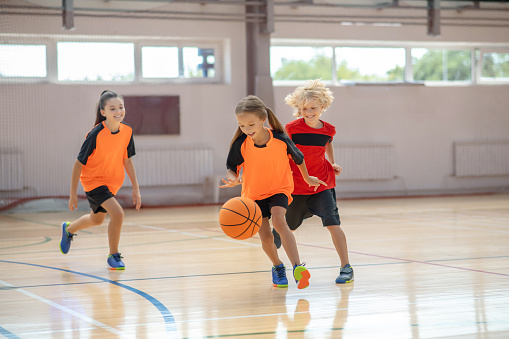 Niños con ropa deportiva brillante jugando al baloncesto y corriendo después de la pelota photo