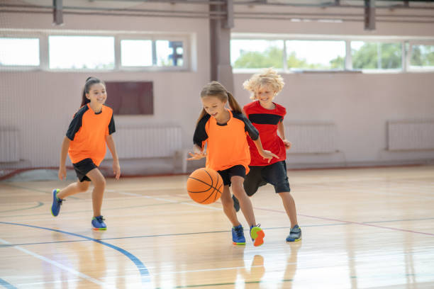 bambini in abbigliamento sportivo brillante che giocano a basket e corrono dietro alla palla - childhood foto e immagini stock