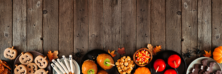 Rustic Halloween treat bottom border over a dark wood banner background with copy space. Above view. Variety of candied apples, cookies, candy and sweets.
