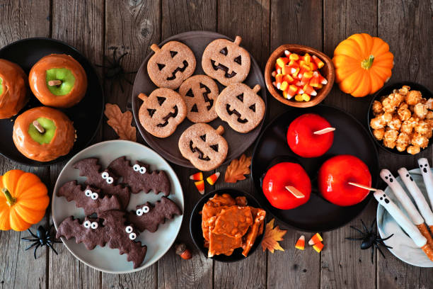 Rustic Halloween treat table scene, top view over a dark wood background Rustic Halloween treat table scene over a dark wood background. Top view. Variety of candied apples, cookies, candy and sweets. snack stock pictures, royalty-free photos & images