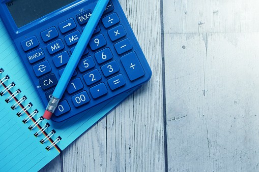 Close up of blue calculator and notepad on color background .