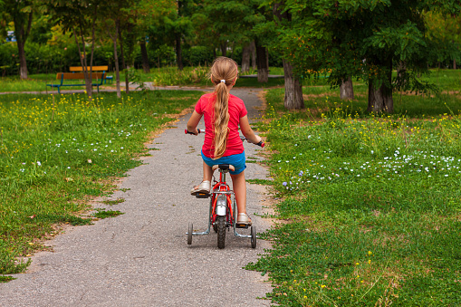 Child riding on bicycle. Blonde smiling girl on red bike on asphalt road in summer. Active lifestyle leisure, physical training on sports stadium. Happy childhood. Kid bicyclist.