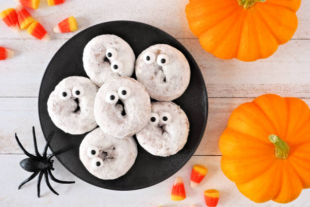 Halloween ghost donuts, top view with pumpkins over white wood