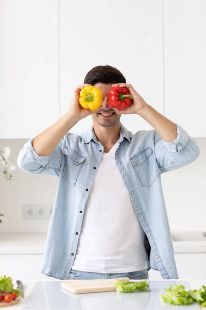 istock Handsome young man holding fresh yellow and red pepper and smiling while standing in the kitchen. 1271200802