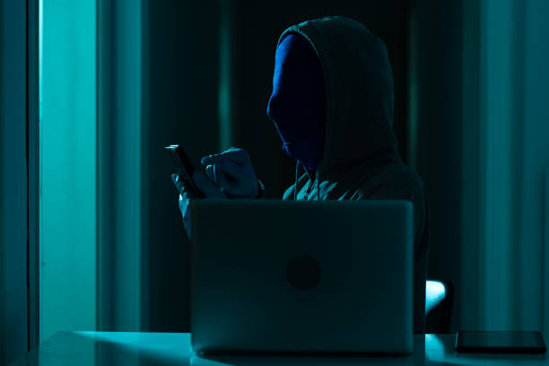 istock Man Wearing Hooded Shirt And Mask Using Laptop In Dark To Hack 1271207032