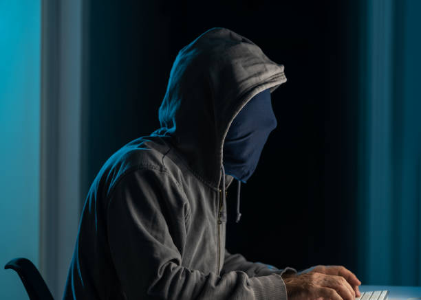 istock Man Wearing Hooded Shirt And Mask Using Laptop In Dark To Hack 1271207526