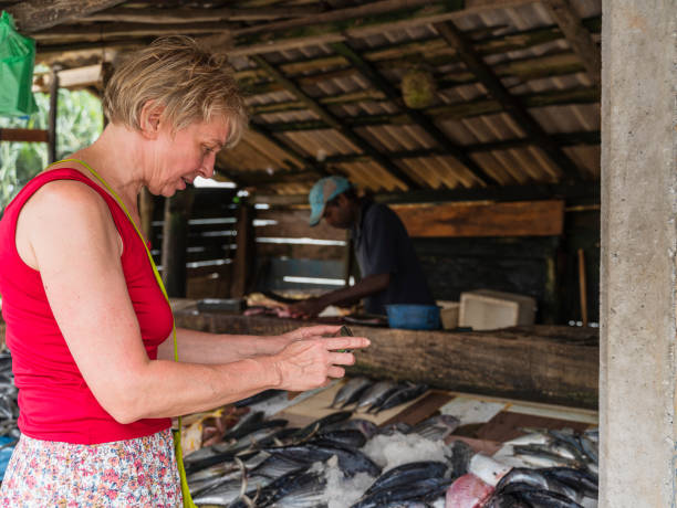 una donna caucasica matura di 55 anni utilizza uno smartphone per scattare foto del pescato fresco in un mercato ittico locale in sri lanka. - women mature adult 50 55 years 50s foto e immagini stock