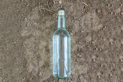 top view of bottle with crystalline liquor like vodka, tequila or mezcal on fertile land