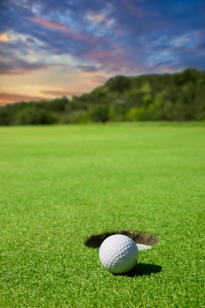 golfball am lochrand bei sonnenuntergang - golf golf flag sunset flag stock-fotos und bilder