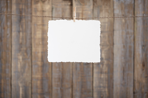 Horizontal deckle edge watercolour paper hanging by a peg and string in front of an old, brown wooden background.
