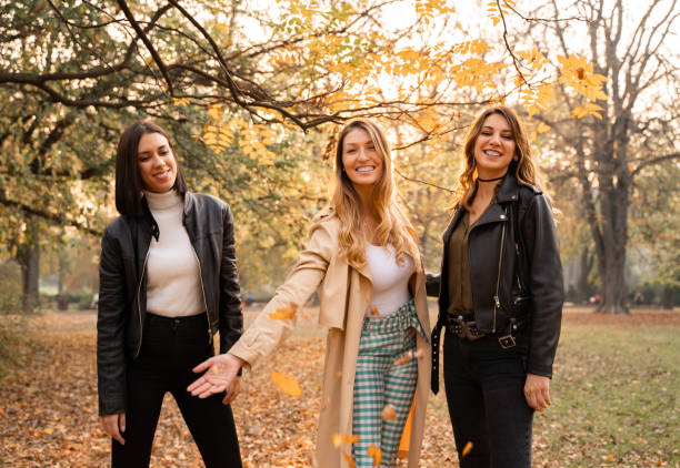 Beautiful same age girls in autumn park, throwing leaves and smiling,fashionable girlfriends enjoying autumn day
