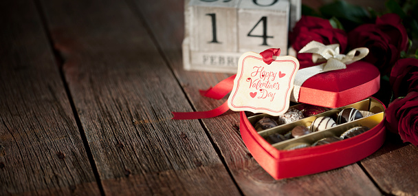 Valentine's day box of chocolates and red roses with a gift tag on a wood background.