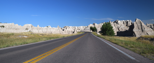 An empty road heads into the rock formations of Badlands National Park under a clear blue sky.