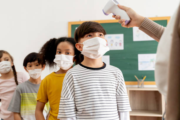 istock Group of diverse students in school building checked and scanned for temperature check. Elementary pupils are wearing a face mask and line up before entering into classroom. 1271251955