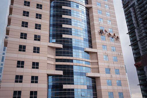Dubai / United Arab Emirates - February 1, 2020: Group of men hanging very high while cleaning windows of skyscraper in Dubai, United Arab Emirates