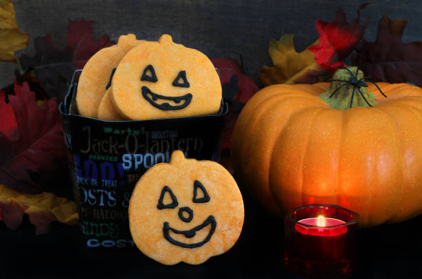 biscotti a forma di zucca in un secchio di halloween in un ambiente autunnale, immagine a bassa luce con candela accesa. - biscuit red blue macro foto e immagini stock