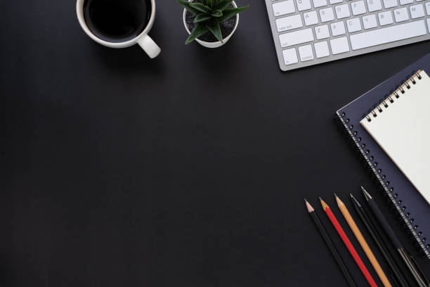 istock Top view above of Black office desk table with keyboard, notebook and coffee cup with equipment other office supplies. Business and finance concept. Workplace, Flat lay with blank copy space. 1271261109