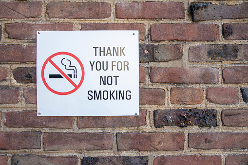 no smoking red white black sign screw onto a red brick wall