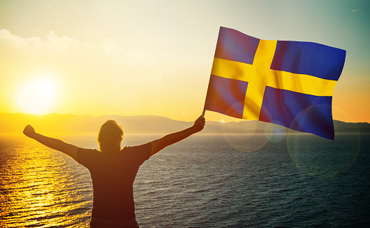 The man is waving the Swedish Flag against the sunrise. Patriotism concept. Horizontal composition with copy space.
