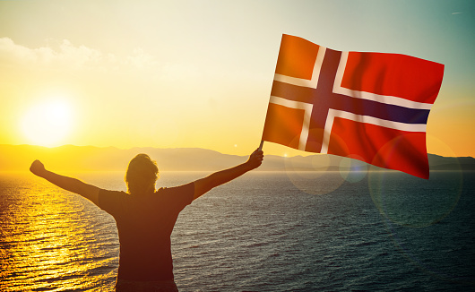 The man is waving the Norwegian Flag against the sunrise. Patriotism concept. Horizontal composition with copy space.