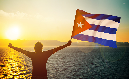 The man is waving the Cuban Flag against the sunrise. Patriotism concept. Horizontal composition with copy space.