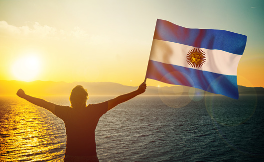 The man is waving the Argentinian Flag against the sunrise. Patriotism concept. Horizontal composition with copy space.