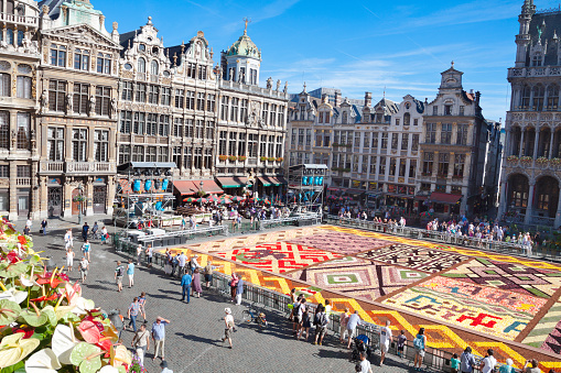 Aerial view of half Grand Place in Brussels with flower carpet and buildings. Many people and tourists are walking around flower carpet. Flower carpet is regularily event on square and free tourist attraction