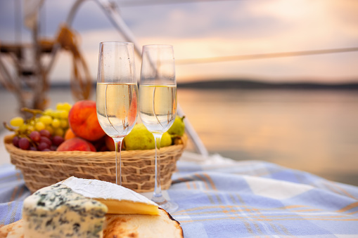 picnic on a yacht at sunset closeup glasses of champagne, fruit basket and bread with cheese