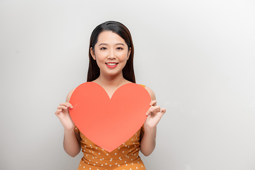 Attractive young asian woman showing red heart on white background