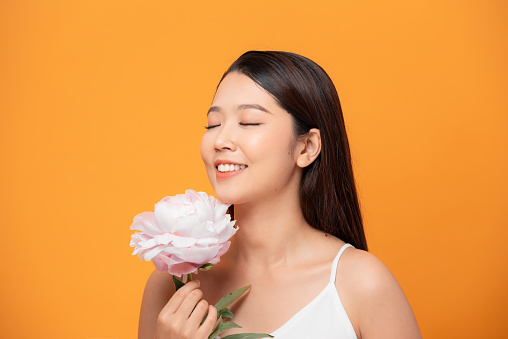 Young woman sniffing pink peony flower closed her eyes on yellow background