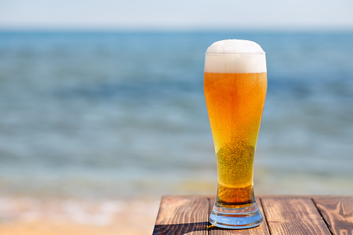 glass of light beer with froth and bubbles at the edge of table with sea on the background
