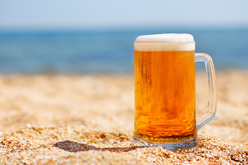 mug of light beer with froth and bubbles on the sea beach