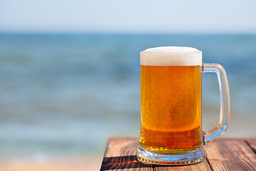 mug of beer with froth and bubbles at the edge of table with sea on the background