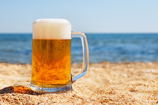 mug of light beer with froth and bubbles on the sea beach