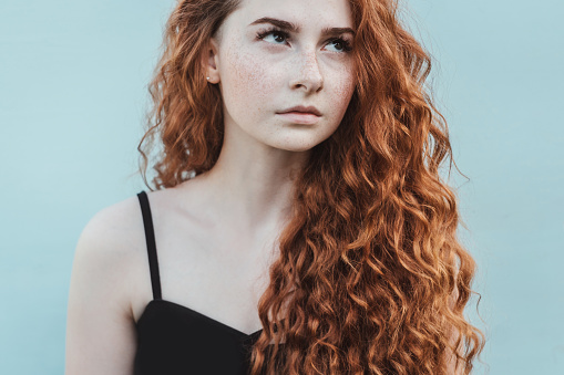Portrait of cute ginger girl with red curly hair on blue background.