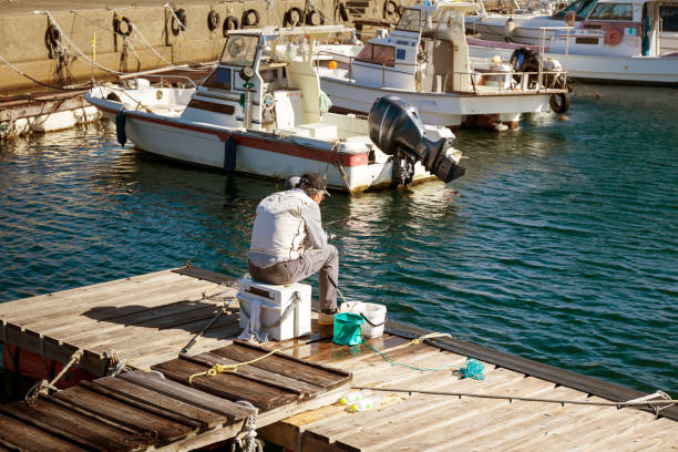 Beppu, Oita Prefecture, Kyushu island, Japan, November 11, 2017: an elderly Japanese man catches fish sitting on a wooden pier by the water